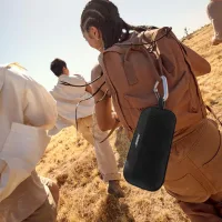 Yürüyüşte sırt çantasına asılmış siyah Bluetooth hoparlör
